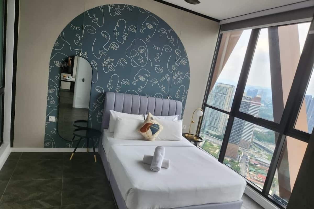 Un dormitorio moderno con una cama grande, una pared curva con un diseño facial, vistas de la ciudad a través de amplios ventanales y una mesita de noche con una lámpara.