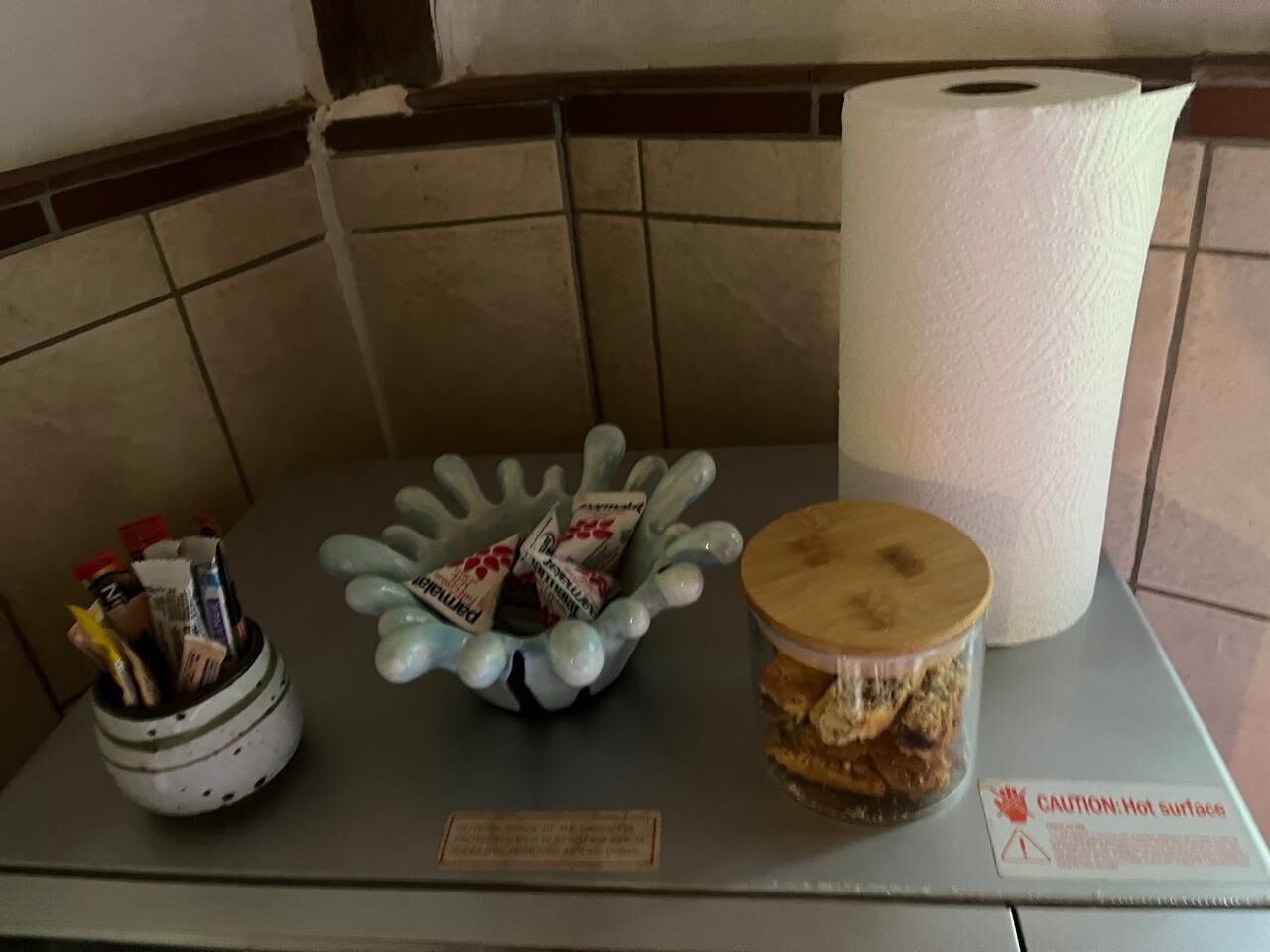 A table with a container of pens, a decorative bowl with chocolates, and a jar of cookies.