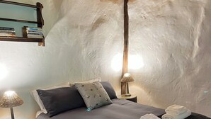 A bedroom with a bed, pillows, a bedside lamp, a small table, and a wall-mounted shelf with books. - Enchanting Forest Cottage in Hogsback, village of beautiful hikes and waterfalls (Hogsback)