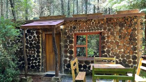 A rustic cabin with a stone wall, wooden door, and bench seating area. - Enchanting Forest Cottage in Hogsback, village of beautiful hikes and waterfalls (Hogsback)