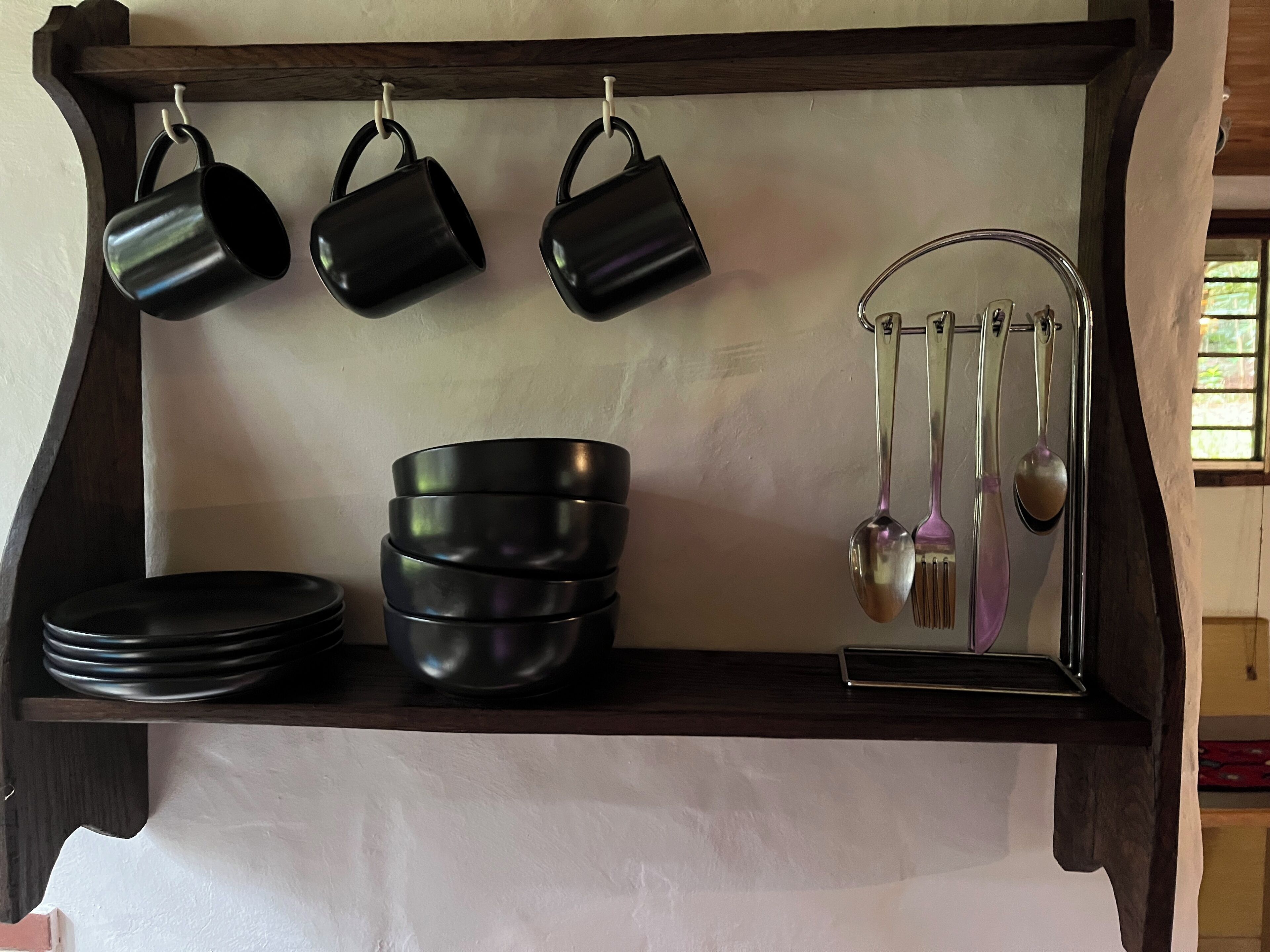 Una estantería en la cocina con tazas, cuencos y utensilios negros.