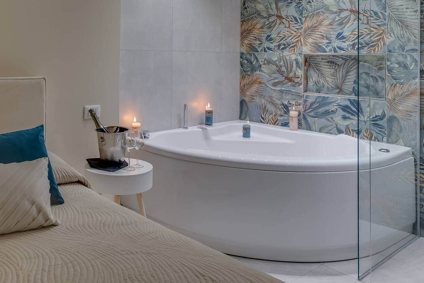 Un bagno moderno con una vasca freestanding, un comodino con una candela e un pannello di vetro decorativo.