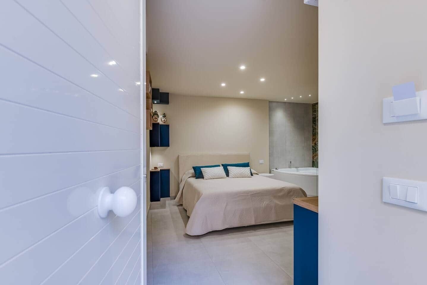 A modern bedroom with a bed, bedside tables, a built-in shelf, and a large window.