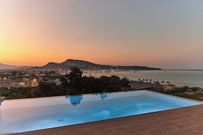 Une piscine à débordement offrant une vue sur le paysage urbain et sur une étendue d’eau au coucher du soleil.
