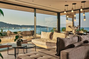 Ein modernes Wohnzimmer mit einer großen Glaswand und einem herrlichen Blick auf das Meer und die Hügel.