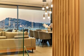 Ein modernes Interieur mit einer Couch, Stühlen, einem Esstisch und Blick auf eine Stadtkulisse durch große Fenster.