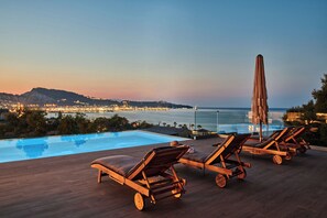 Ein Poolbereich mit Liegestühlen und Blick auf das Meer und die Stadtlichter im Abenddämmerung.