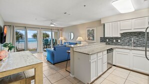 A modern kitchen with white cabinets, a granite countertop, and a view to the outside. - Windancer 208 Gulf Front, Free Beach Service, Emerald Waters, Pool, & Grill. (Miramar Beach)