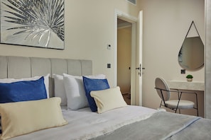 A hotel room with a bed, pillows, a desk, a chair, a mirror, and a wall art piece. - Althea Suite - A Lavish Seaview Suite, suite (ZAKYNTHOS)