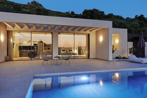 Una casa moderna con piscina, amplios ventanales y un patio con mobiliario.