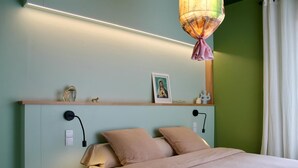 Un dormitorio con cama, lámparas de noche, un estante con adornos y una lámpara colgante.