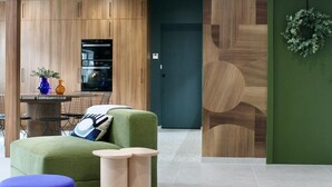 Un interior moderno con diseño de pared de madera, una puerta verde y una zona de estar con un otoman azul.