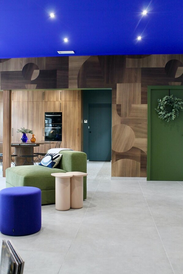 A modern interior with a wooden wall design, a green door, and a seating area with a blue ottoman.