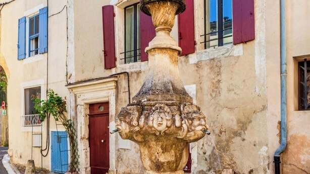 Un edificio histórico con una fuente en primer plano, que presenta una estructura de piedra con un adorno en la parte superior.
