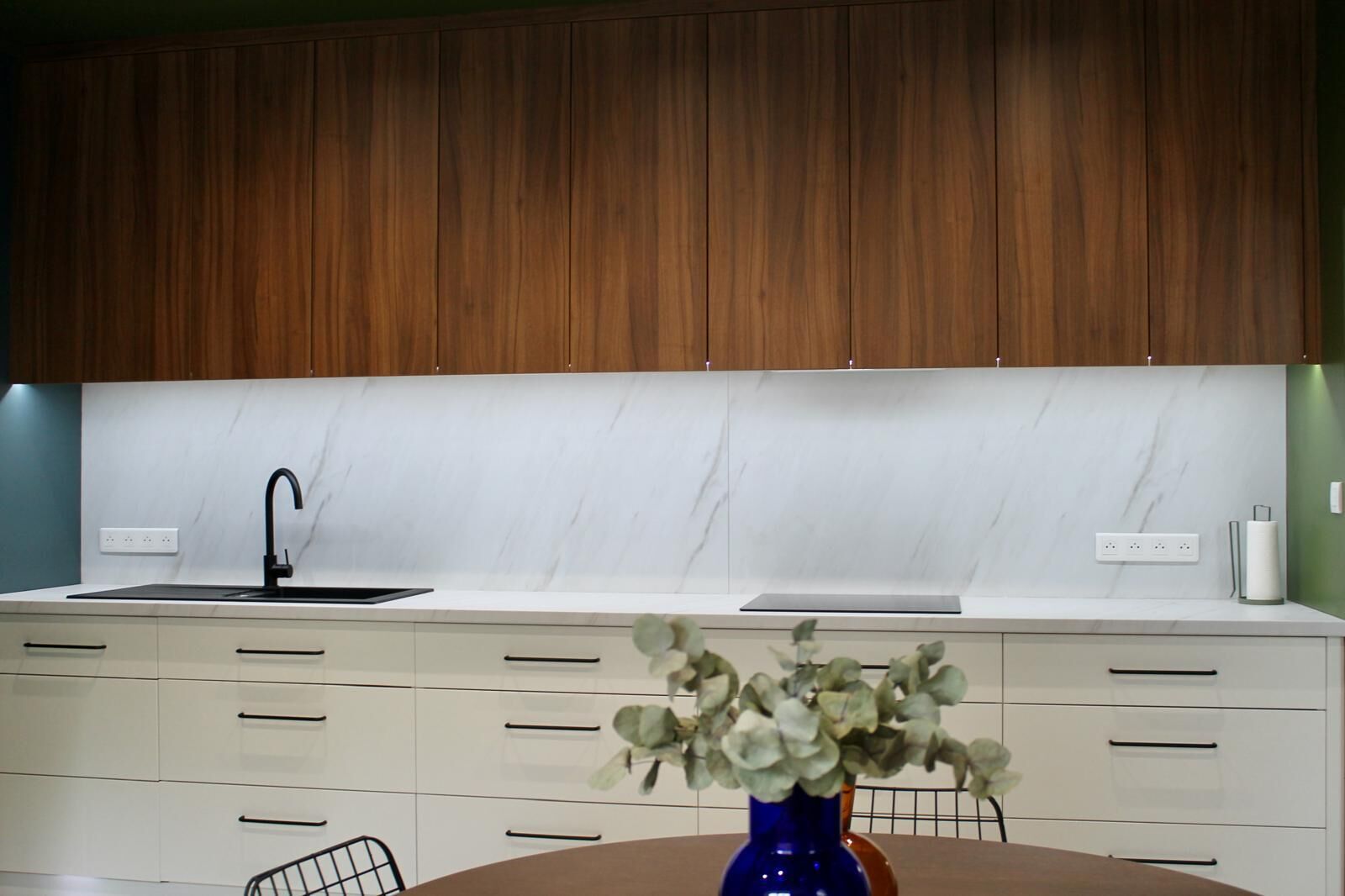 Une cuisine moderne avec des meubles en bois, un pare-feu en marbre blanc, un robinet noir et un vase rempli de fleurs posé sur le plan de travail.