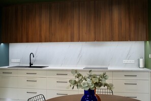 A modern kitchen with wooden cabinets, a white marble backsplash, a black faucet, and a vase with flowers on the counter.