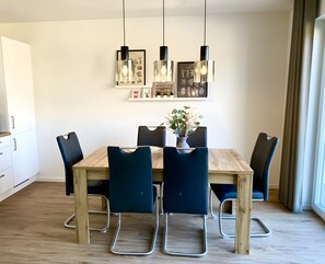 A dining area with a wooden table, six chairs, pendant lights, and wall-mounted artwork. - Holiday Home Mena at Lake Diemelsee (Diemelsee)