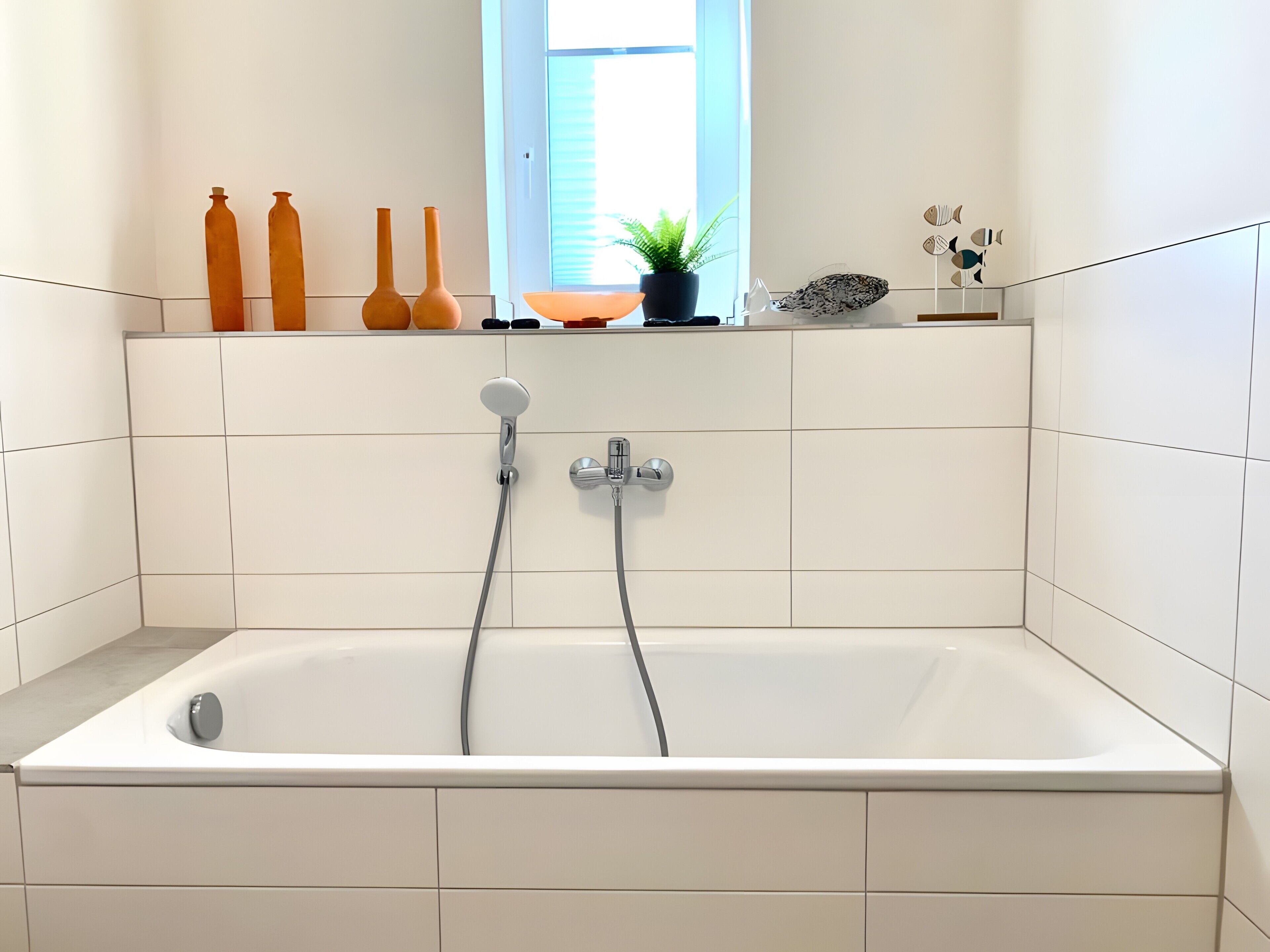Ett modernt badrum med badkar, två duschmunstycken, ett fönster och en hylla med dekorativa föremål.
