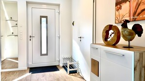 A hallway with a white door, a wooden floor, a white cabinet with decorative items, and a wall-mounted artwork. - Holiday Home Mena at Lake Diemelsee (Diemelsee)