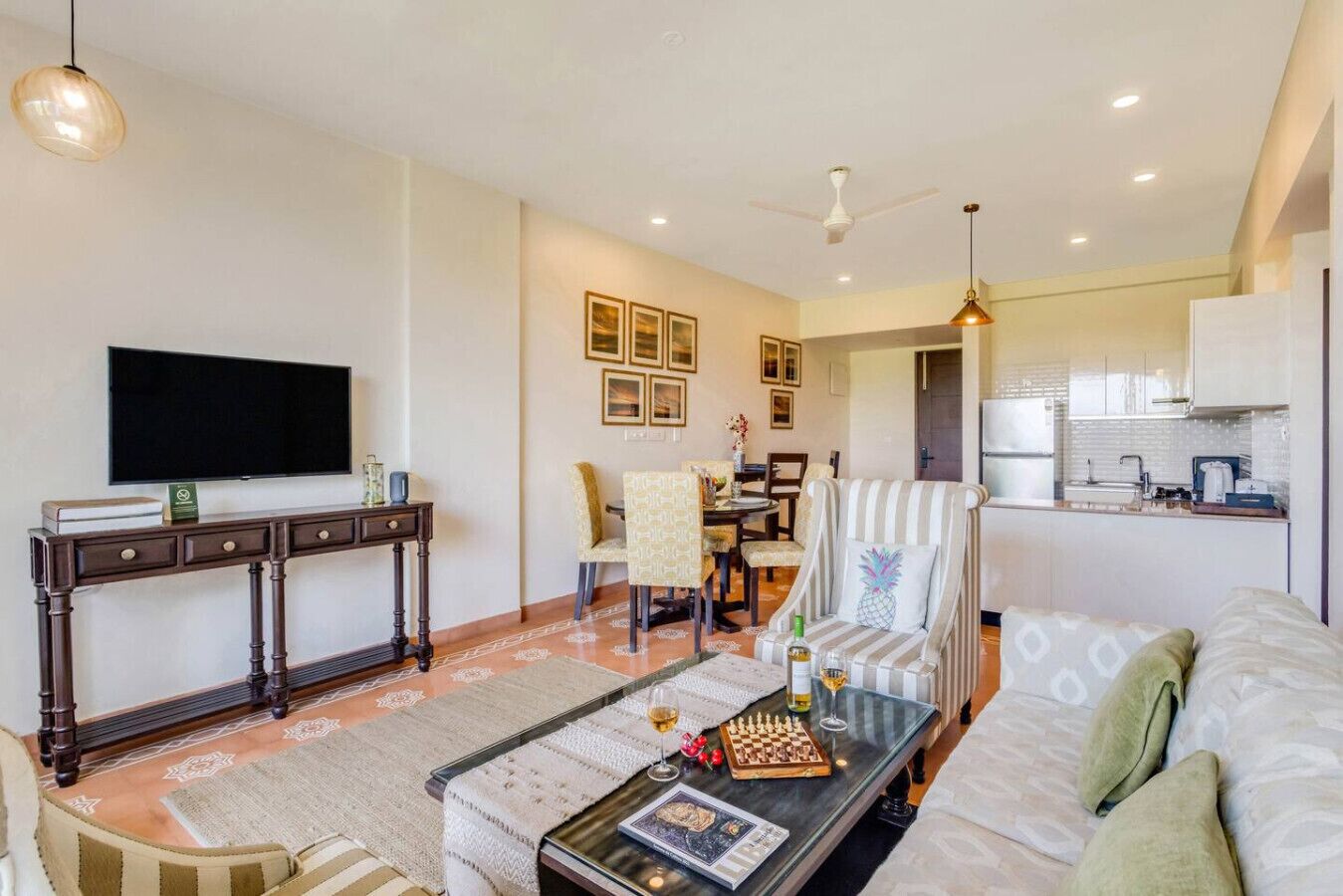 Una sala de estar moderna con un sofá, una mesa de centro y un televisor. Se observa un comedor con sillas y una mesa. La cocina es visible al fondo.