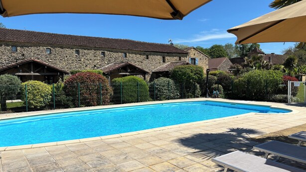 Une piscine entourée de bâtiments en pierre et de verdure, avec des chaises longues et des parasols.