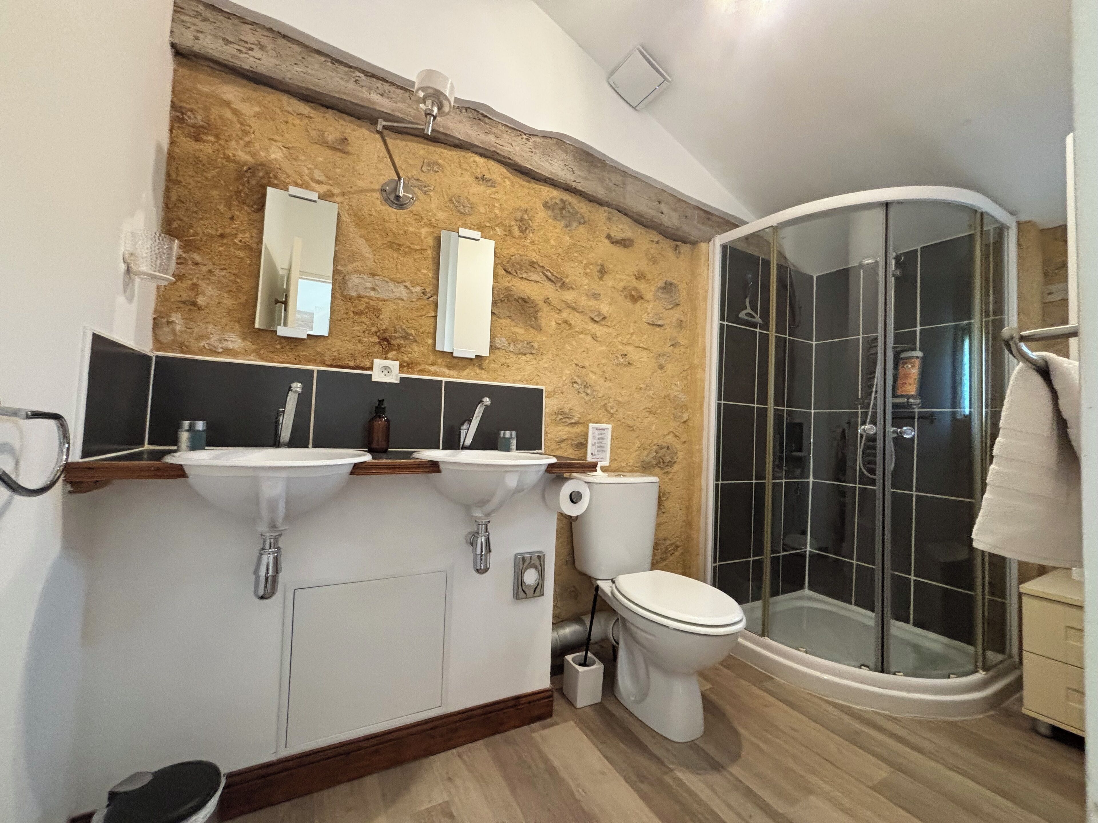 Une salle de bain moderne avec un mur d’accent en bois, deux vasques, des toilettes et une douche à parois de verre.