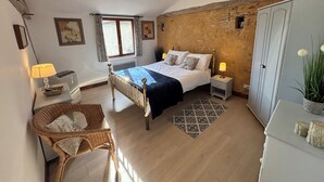Une chambre à coucher comprenant un lit, une chaise, une table de chevet, une lampe, une fenêtre et un ventilateur de plafond.