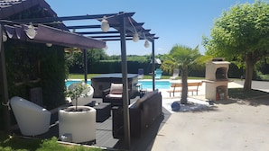 Un espace aménagé au bord de la piscine, comprenant une pergola, des chaises longues, un jacuzzi et un barbecue.