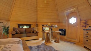 L’intérieur chaleureux d’un chalet avec un plafond en bois, un canapé, une table à manger et une grande fenêtre.