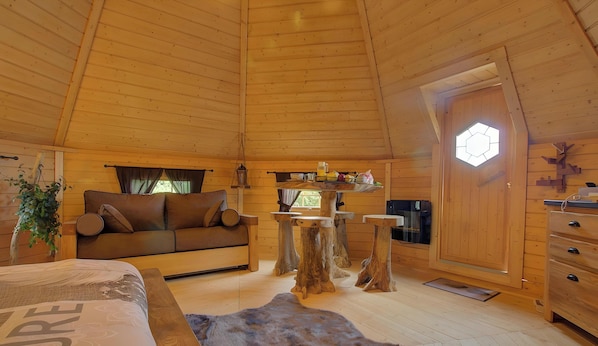 Interior acogedor de una cabaña con techo de madera, un sofá, una mesa de comedor y un ventanal grande.