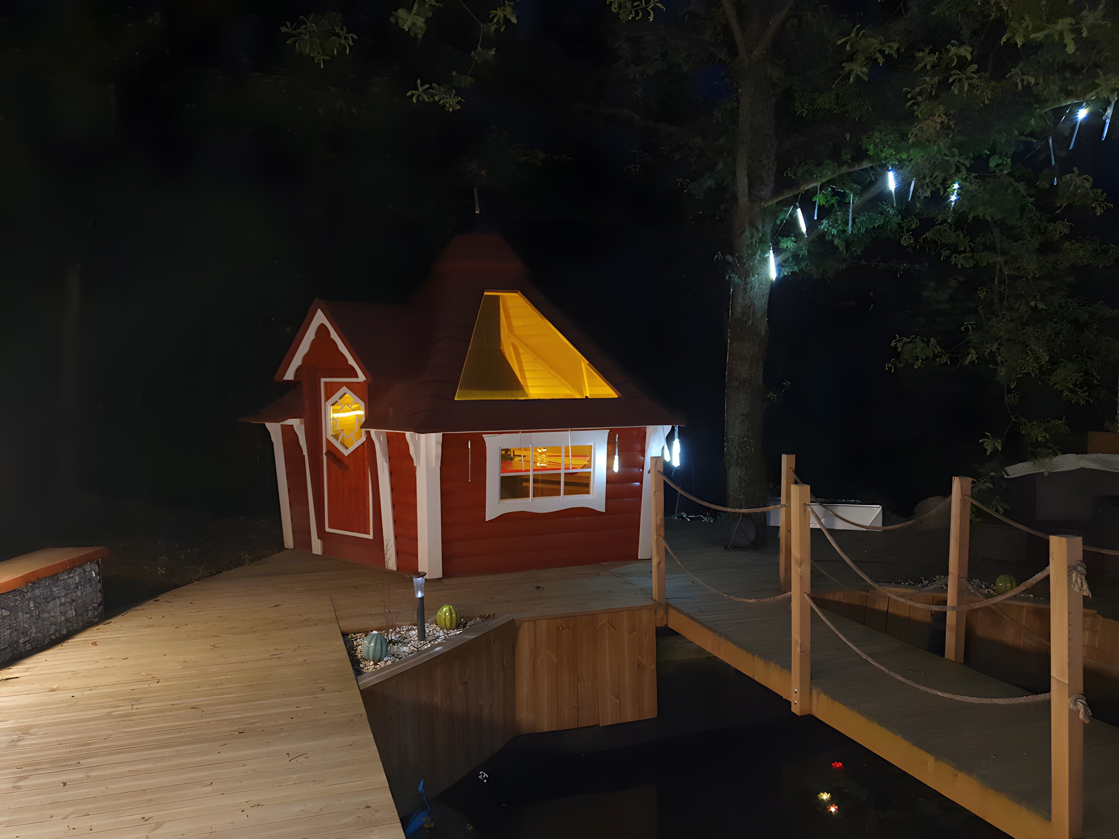 Une petite cabane en bois, à l’extérieur rouge, avec un toit triangulaire et une jetée qui s’avance sur une étendue d’eau.