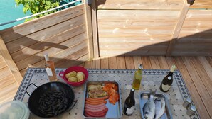 Une terrasse en bois avec une table carrelée, mise pour un repas, comprenant différents plats et bouteilles.
