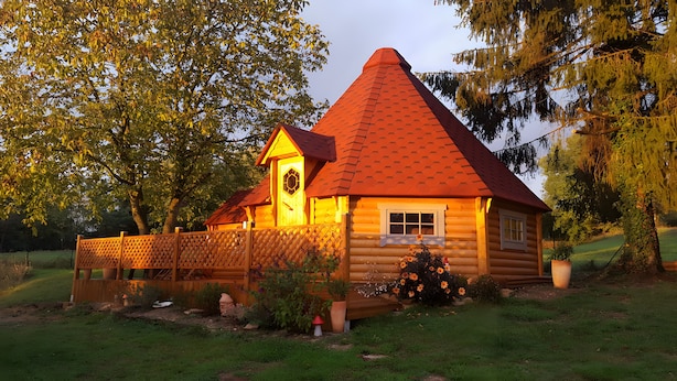 Une cabane en rondins avec un toit conique, une clôture en bois et un jardin fleuri.