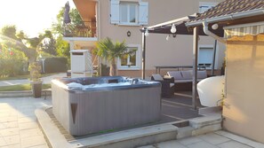Un jacuzzi en un patio trasero con mobiliario exterior y un edificio al fondo.
