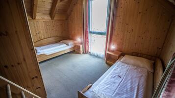 Quarto de cabana de madeira com duas camas simples, uma janela com cortinas e teto de madeira.
