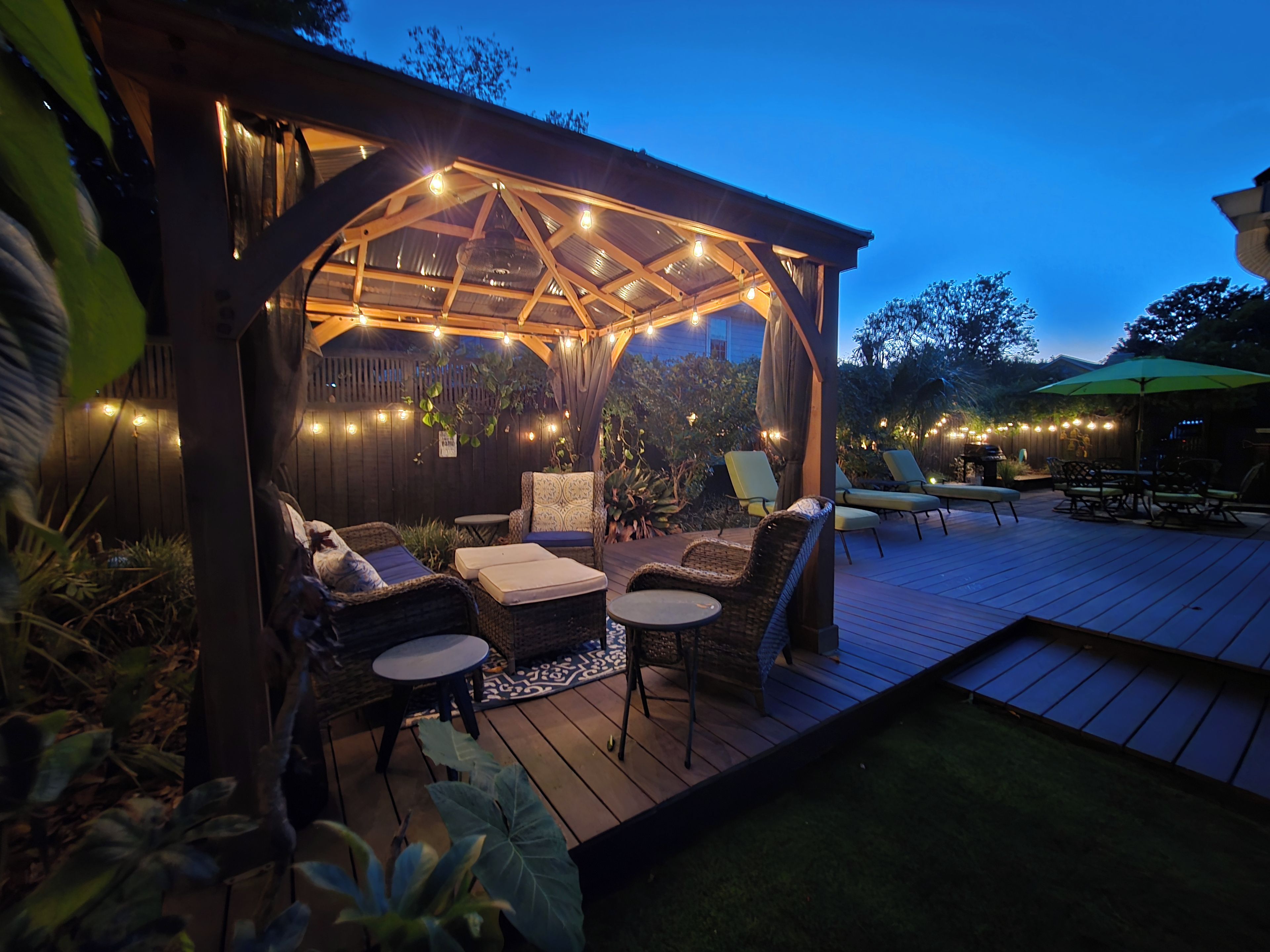 An outdoor patio with a covered seating area, string lights, and a wooden deck.