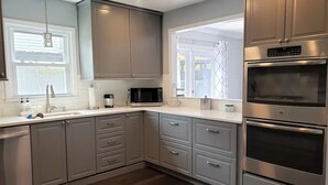 A modern kitchen with grey cabinets, a built-in microwave, and a double oven. - Old Village Home w/ Huge Patio-Beach & CHS in 10 Mins! STR#ST260017 BL#20124322 (Mount Pleasant)
