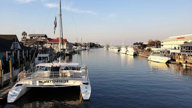 A marina with boats docked, a building with a red roof, and a sign for 'Palmetto Breeze' on a boat. - Old Village Home w/ Huge Patio-Beach & CHS in 10 Mins! STR#ST260017 BL#20124322 (Mount Pleasant)