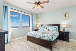 Ein Schlafzimmer mit einem Holzbett, zwei Nachttischen, einem Deckenventilator und einem Fenster mit Jalousien.