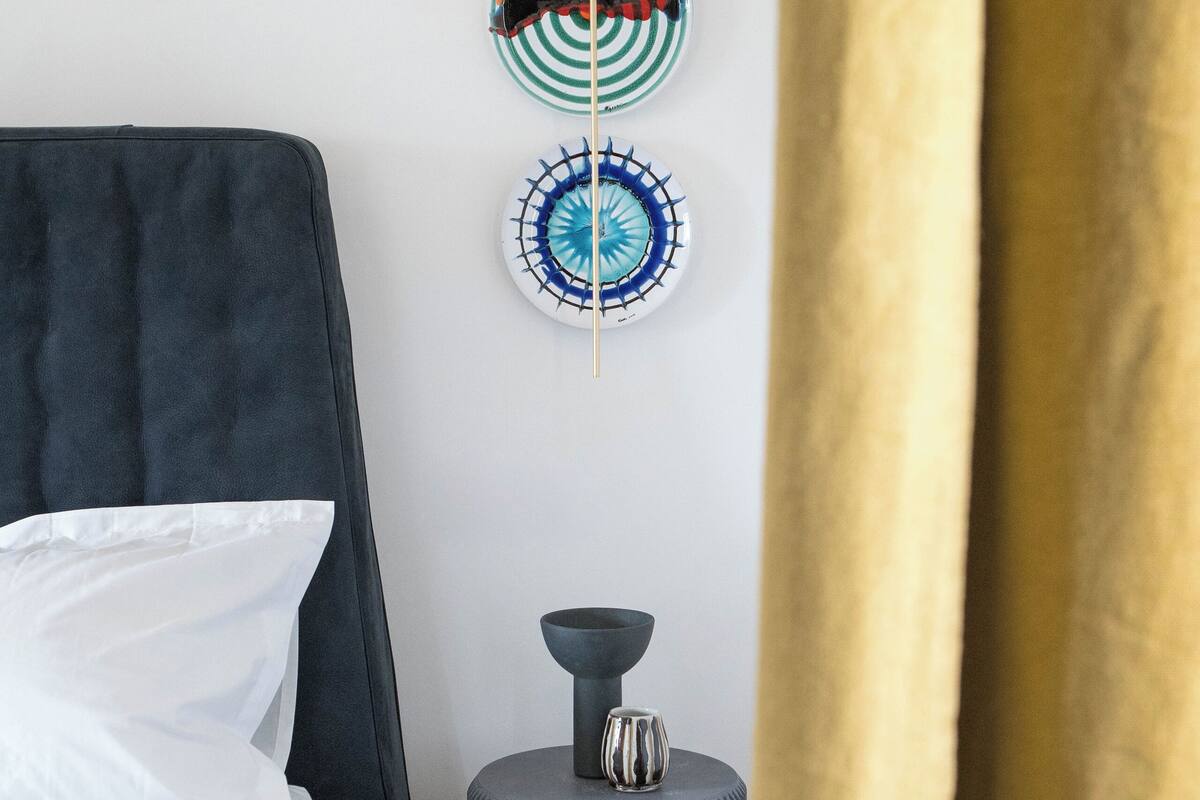 Un dormitorio con cama, una mesita de noche con un florero, y dos placas decorativas en la pared.
