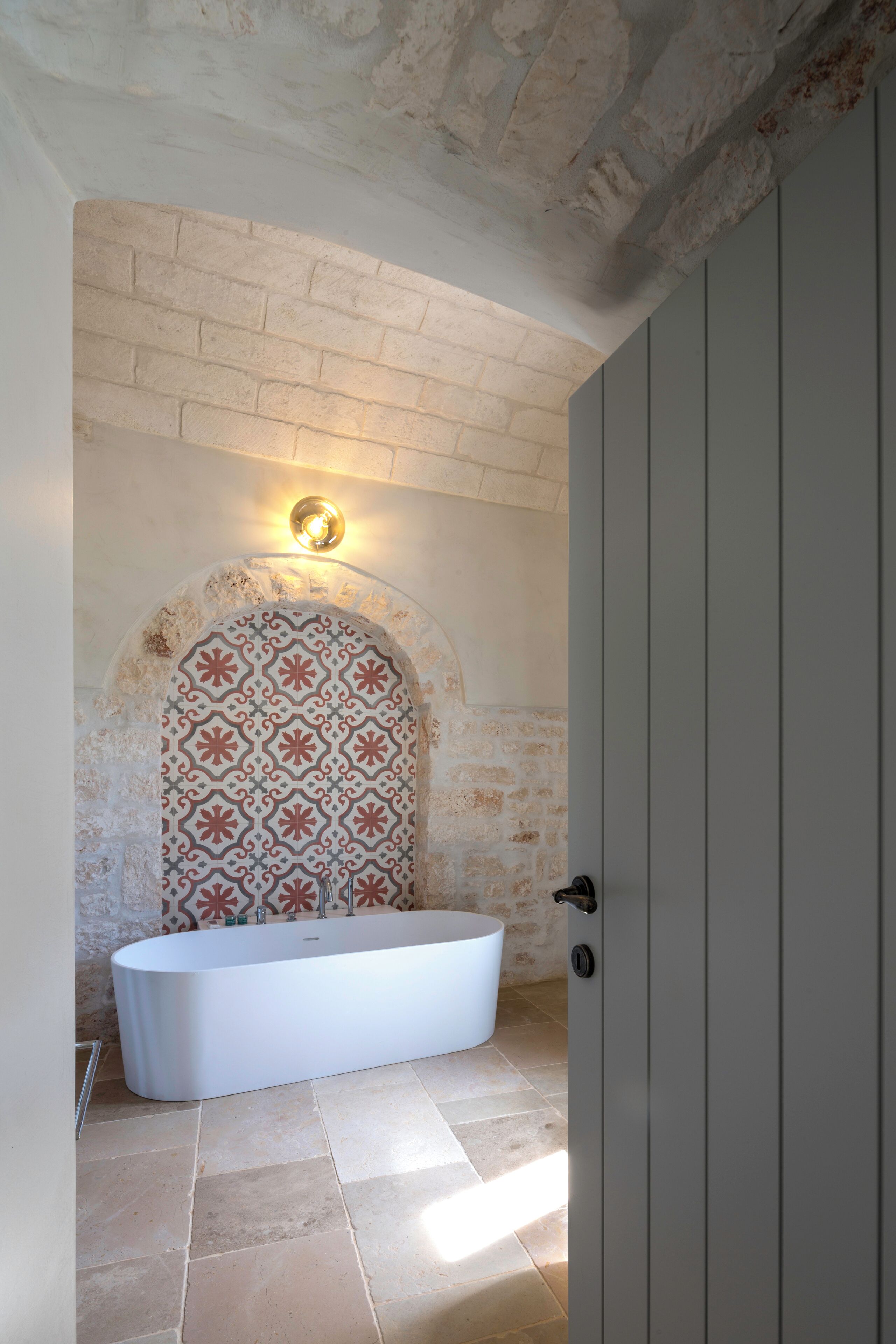 A bathroom with a freestanding bathtub, a patterned archway, and a light fixture above the arch.