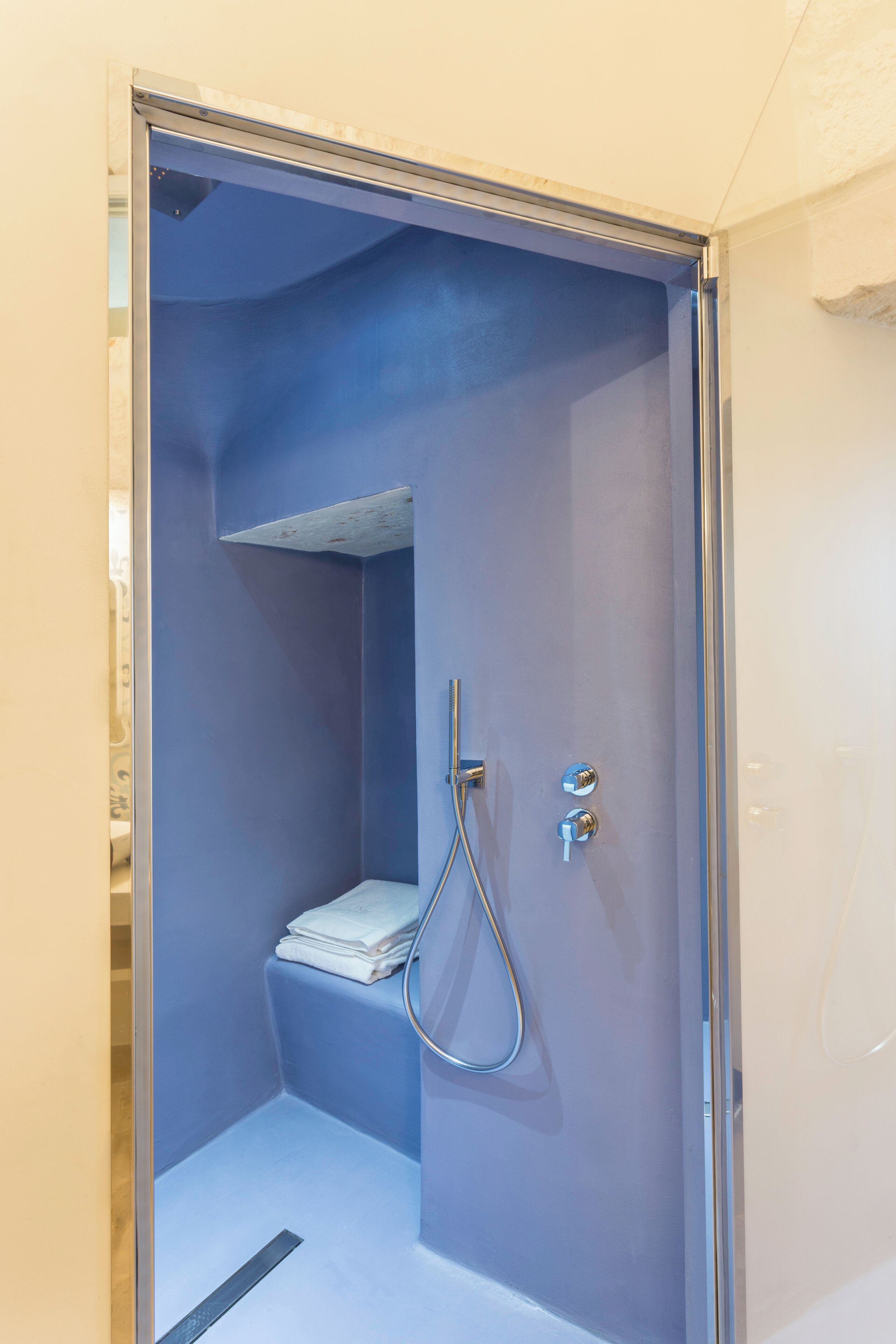 Un espacio de ducha pequeño y cerrado, con una pared azul, un estante y un cabezal de ducha.