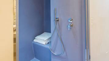 Un espacio de ducha pequeño y cerrado, con una pared azul, un estante y un cabezal de ducha.