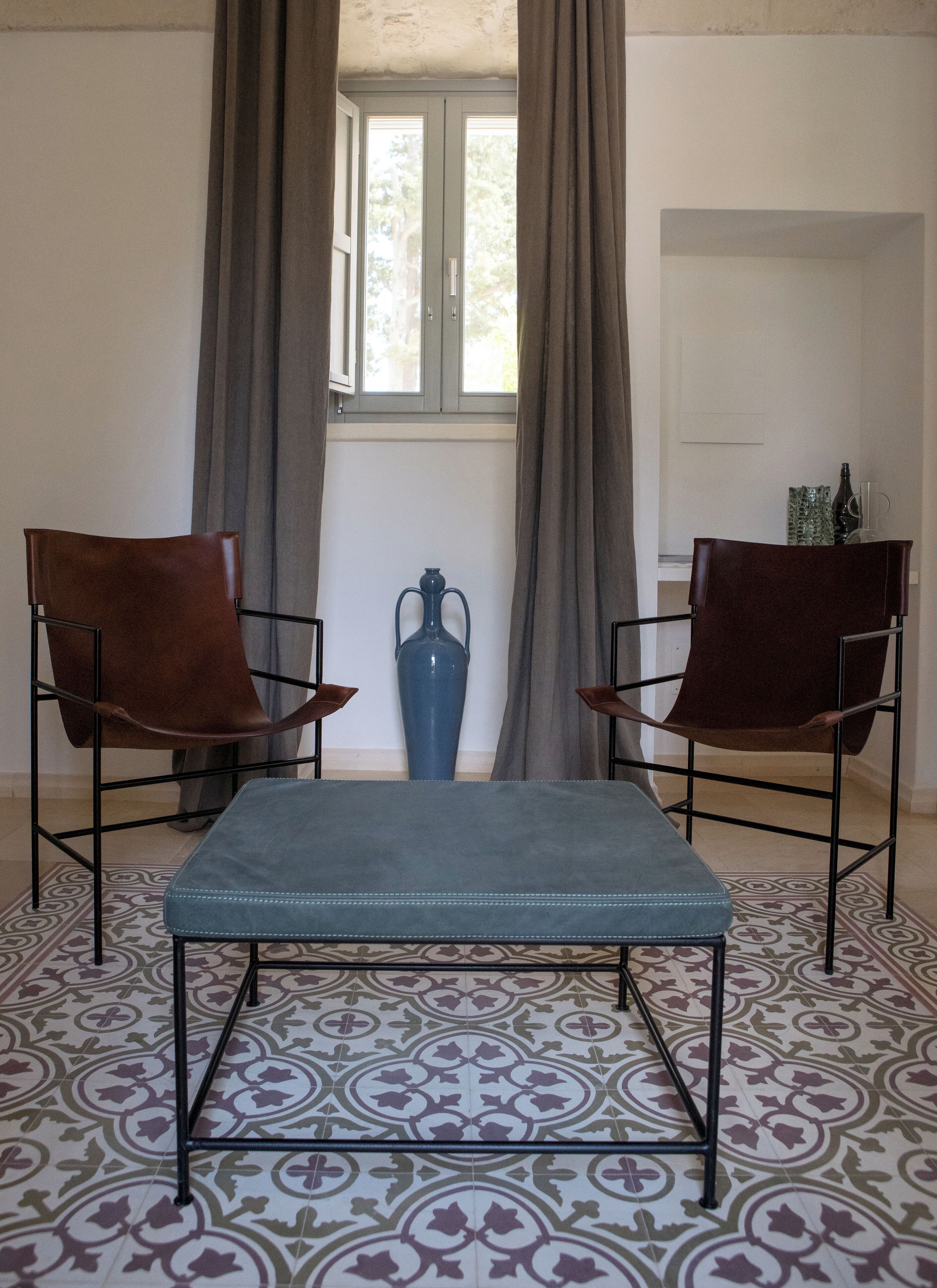 A room with two leather chairs, a blue ottoman, and a decorative vase.