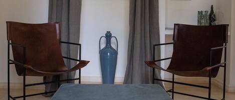 A room with two leather chairs, a blue ottoman, and a decorative vase.