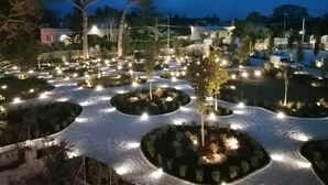 Un área de jardín ajardinado con senderos y árboles, iluminada por luces en el suelo.