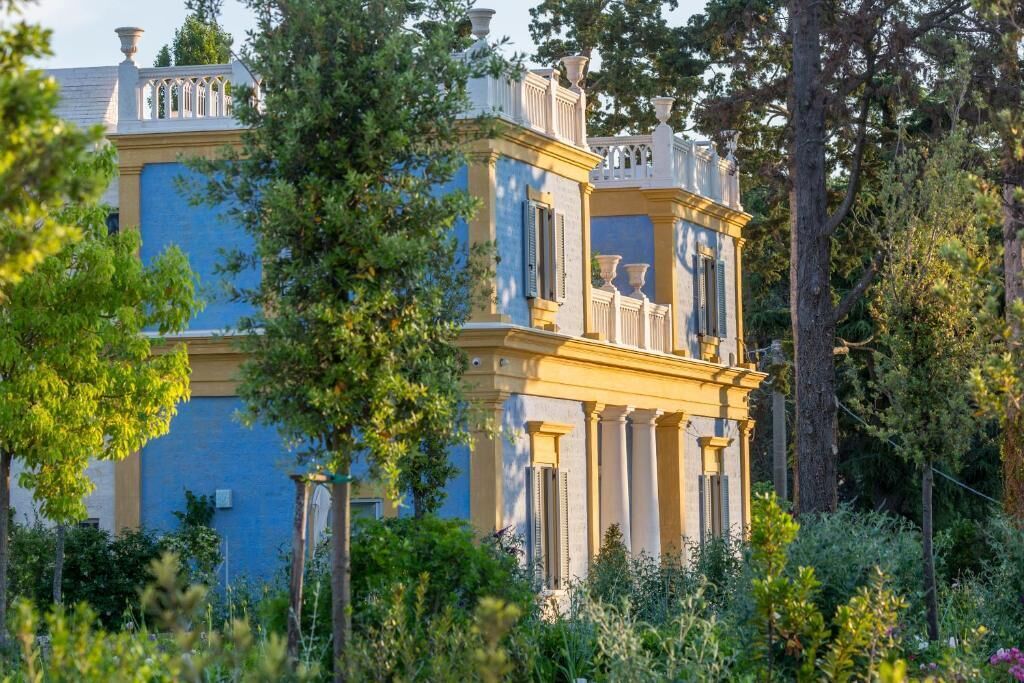 A large, multi-story building with classical architecture, surrounded by lush greenery.