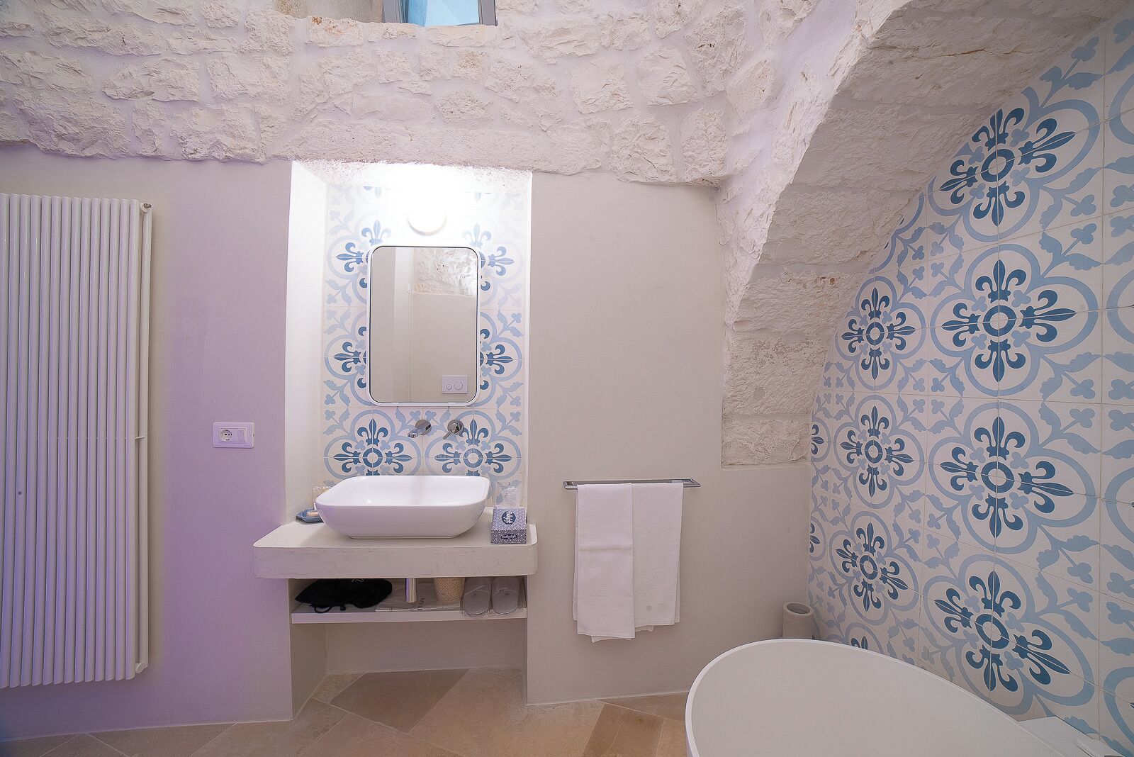 A bathroom with a white sink, a mirror, and a shower. The walls have a blue floral pattern.