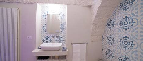 A bathroom with a white sink, a mirror, and a shower. The walls have a blue floral pattern.