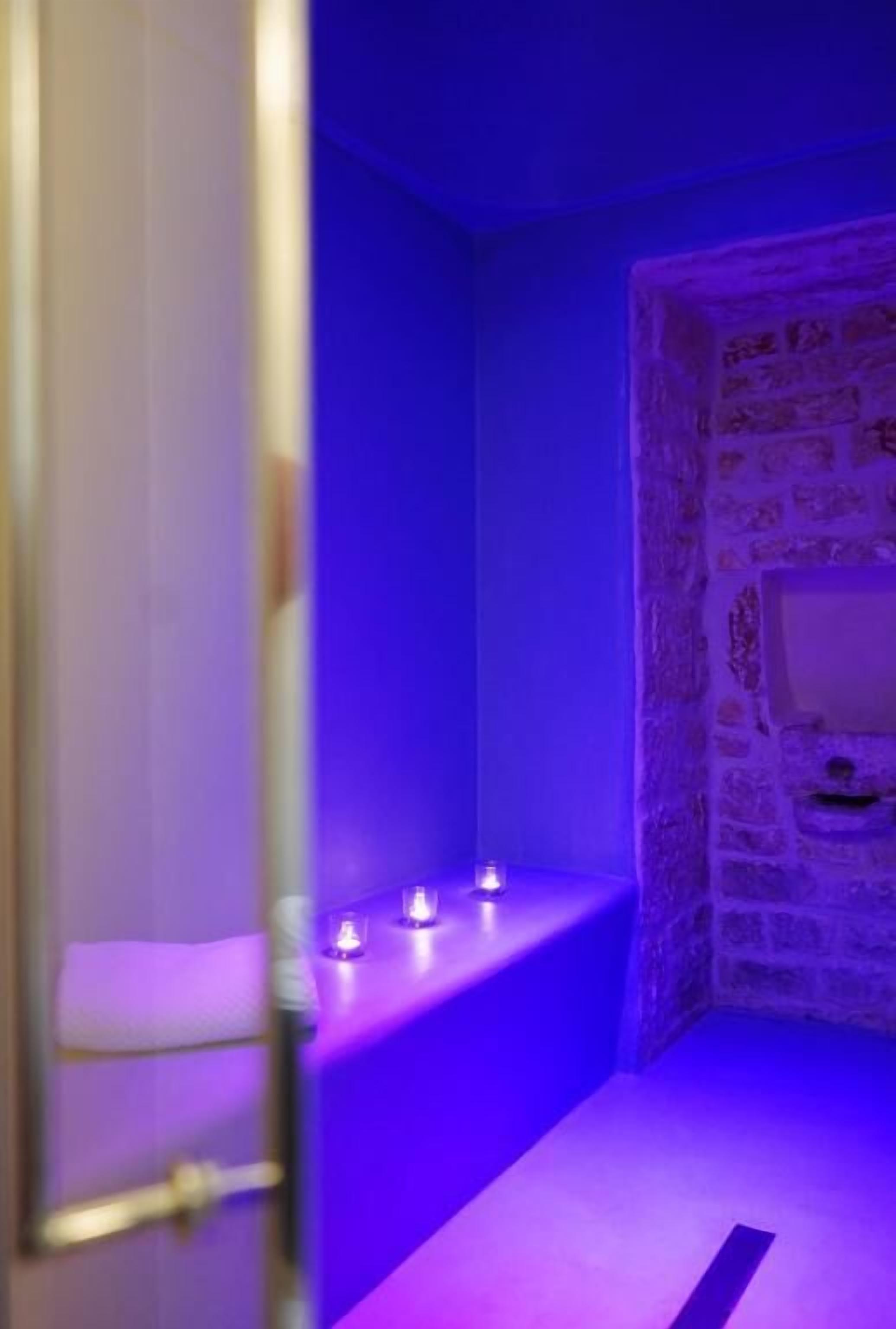 A room with a stone wall, a small sink, and purple lighting.